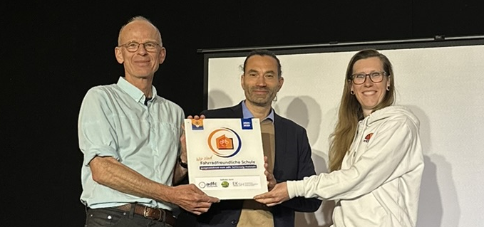 Übergabe Plakette "Fahrradfreundliche Schule" Nora Müller (links) vom ADFC SH übergibt die Plakette "Fahrradfreundliche Schule" an Mathias Kadow-Leder (Schulleiter Holstenschule) und Christian Wagner (Fahrradbeauftrager Holstenschule Neumünster)