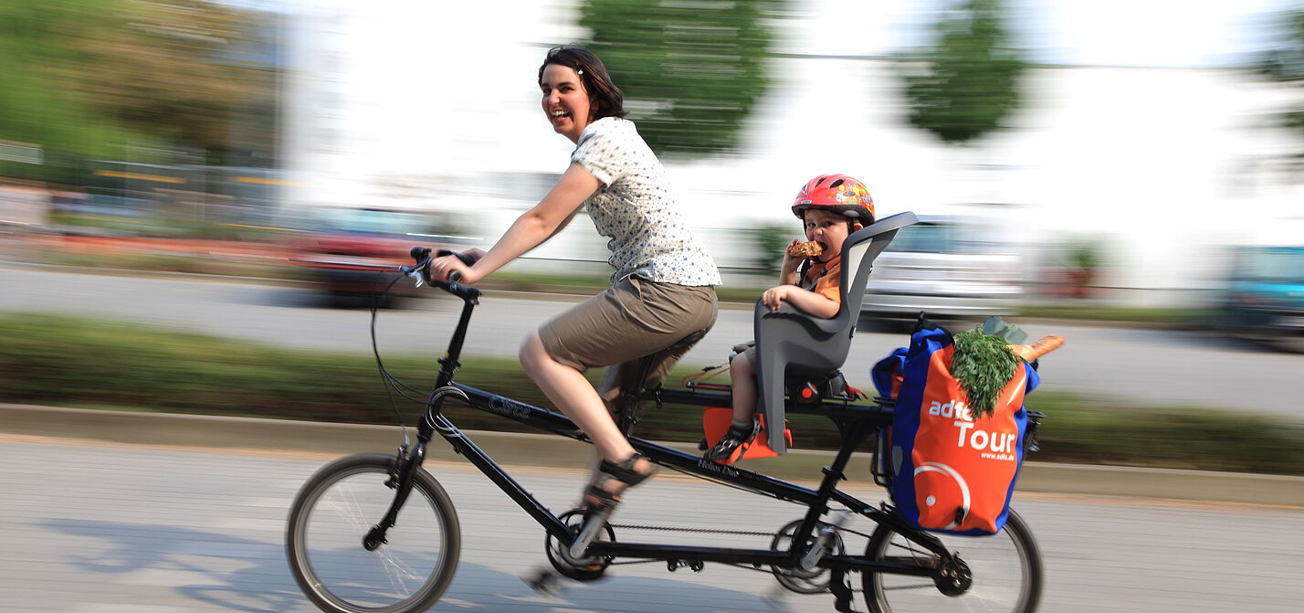 Frau mit Kind und Einkauf auf Lastenrad