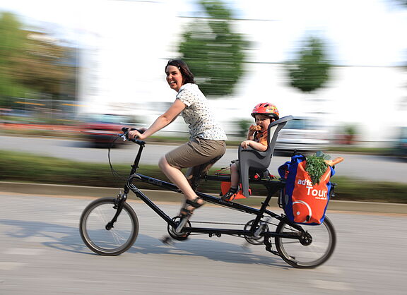 Frau mit Kind und Einkauf auf Lastenrad