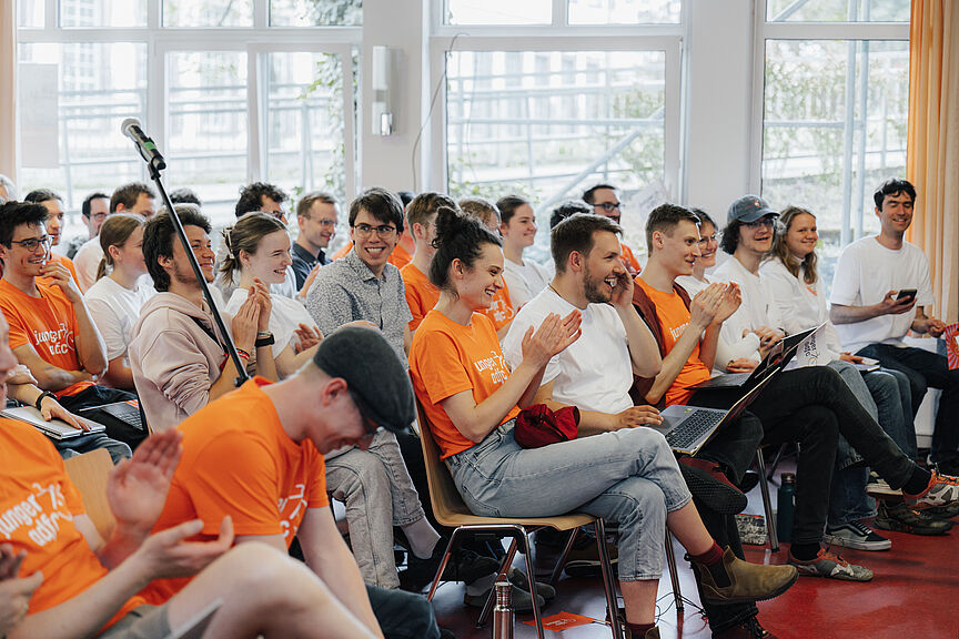 Bundesjugendversammlung des Jungen ADFC Junge Erwachsene sitzen in Stuhlreihen in einem Saal und heben grüne Stimmkarten in die Höhe.