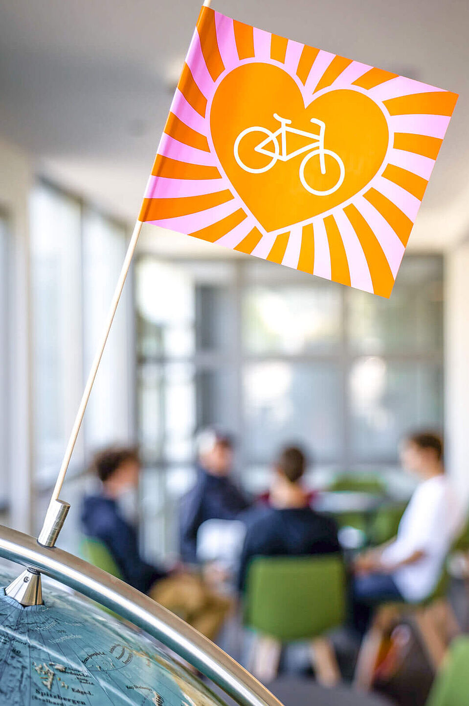 Junger ADFC Eine kleine Fahne mit Herz und Fahrrad steht vor einer Gruppe im Raum.
