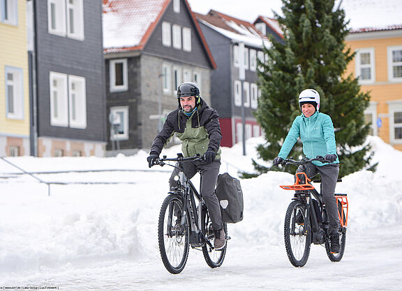 Zwei Radfahrende in verschneiter Stadt. 